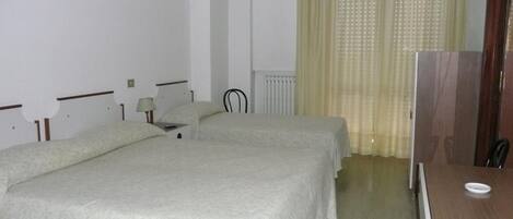 A hotel room with two beds, a desk, a chair, a radiator, and a television.