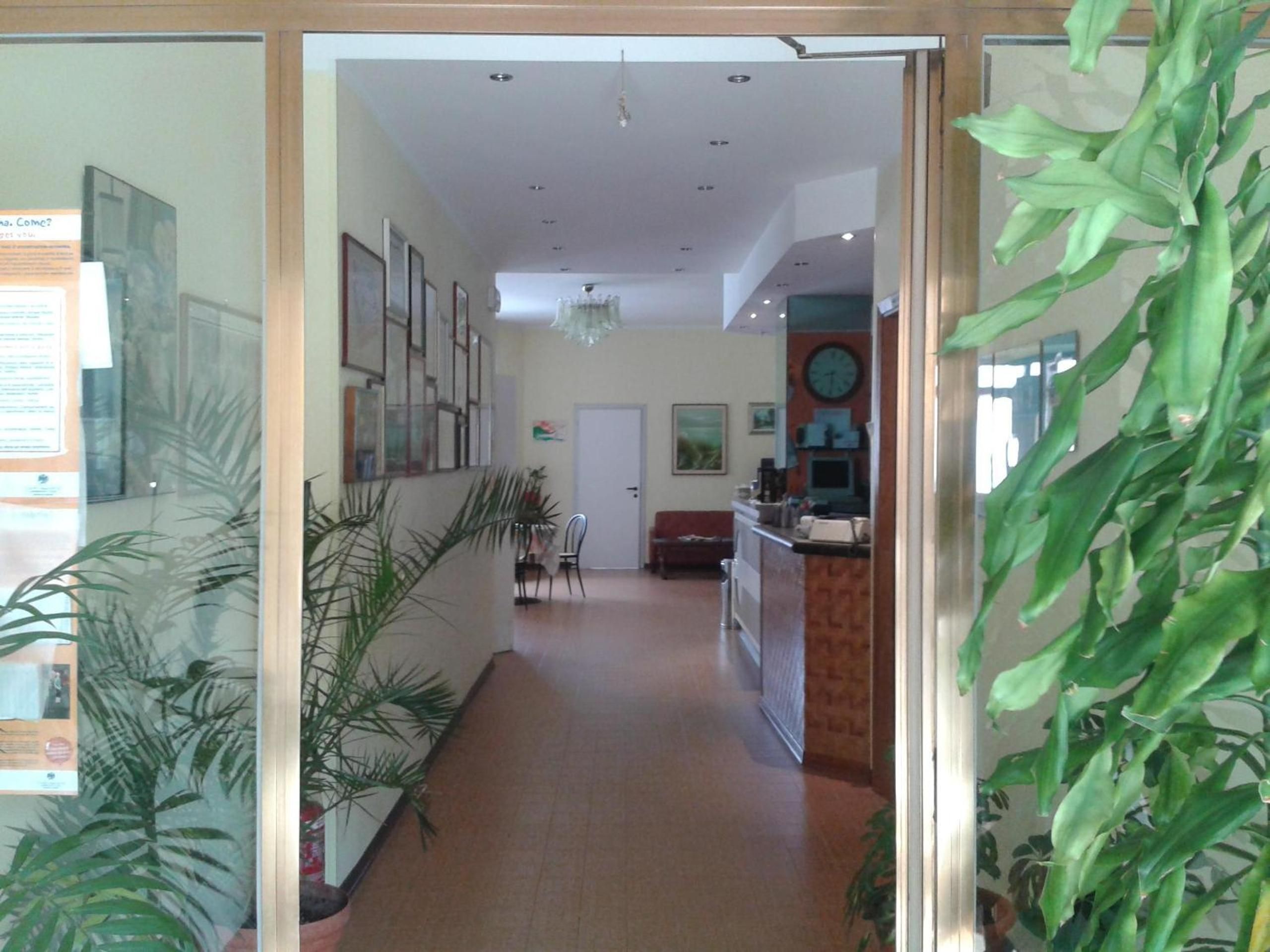 A hallway with a reception desk, chairs, a couch, and framed pictures on the walls.