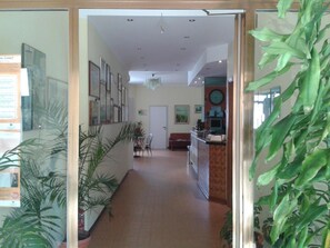A hallway with a reception desk, chairs, a couch, and framed pictures on the walls. - Albergo Tenda Verde (Falconara Marittima)