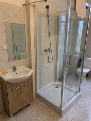 A bathroom with a glass-enclosed shower, a sink with a mirror, and a toilet. - Ow Meduza I Biala Mewa (Międzyzdroje)