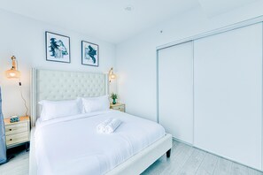 A neatly made bed with white linens and rolled towels, a tufted headboard, bedside lamps, and framed artwork on the wall.