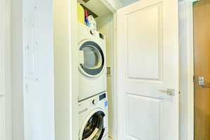 A laundry room with stacked washers and dryers, a wooden door, and a white wall.