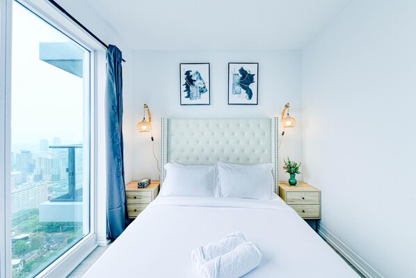 Quarto de hotel com uma cama grande, duas mesas de cabeceira, uma janela com cortinas e duas imagens penduradas na parede.
