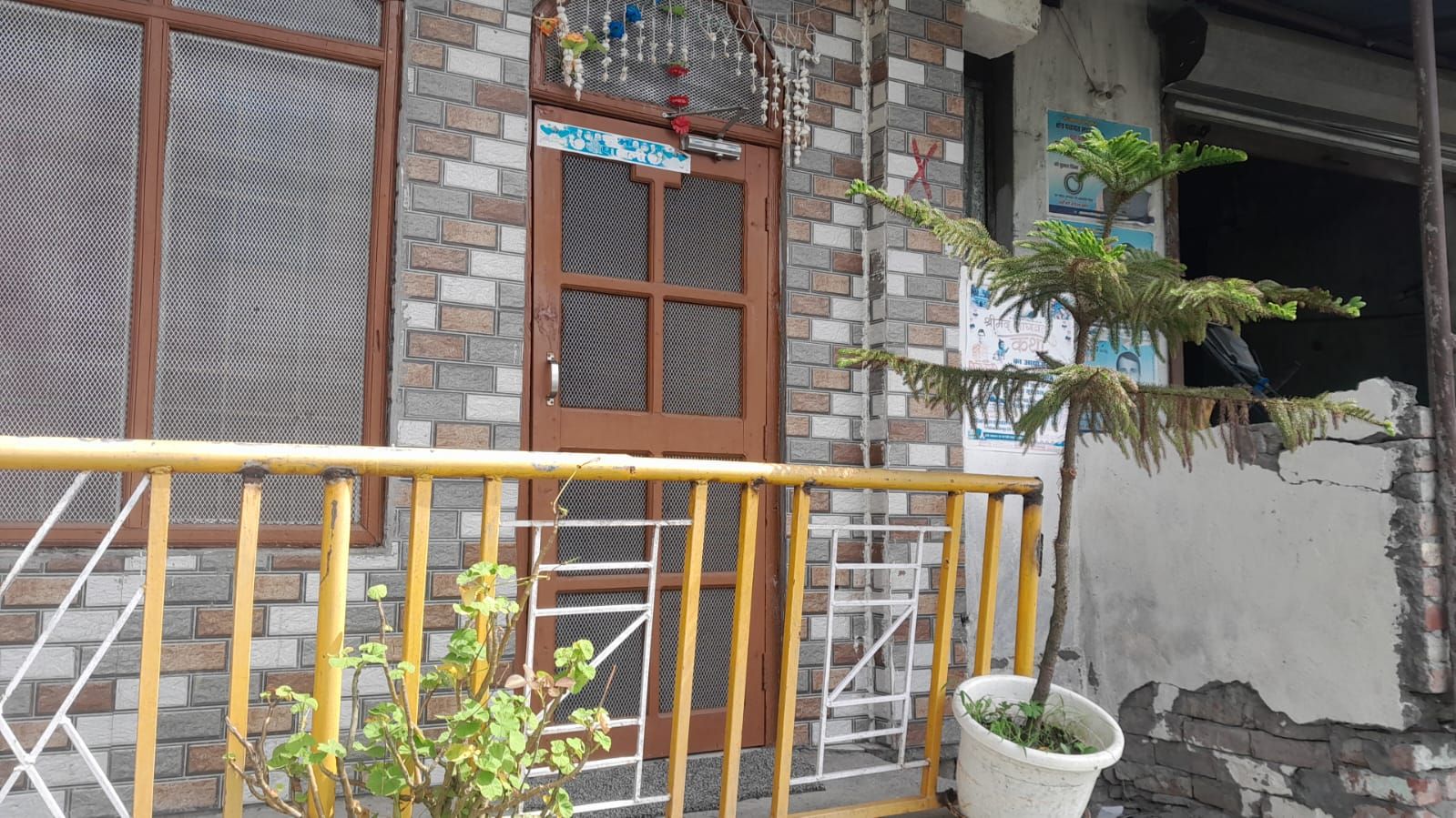 Fachada de edificio con pared de ladrillo, puerta de madera con mosquitera y planta en maceta.