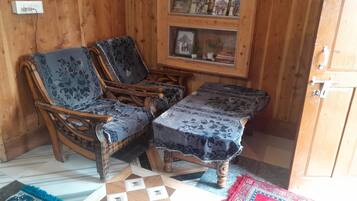 A wooden-paneled room with two upholstered chairs and a small table, a framed picture on the wall, and a patterned rug on the floor.
