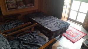 Una habitación con una mesa de comedor de madera, sillas, un tapete rojo estampado y una ventana con persianas.