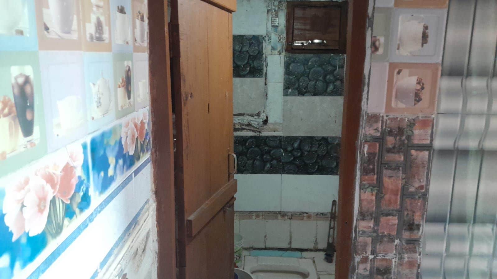 Un pasillo estrecho con una pared de azulejos a un lado y una puerta de madera al otro.
