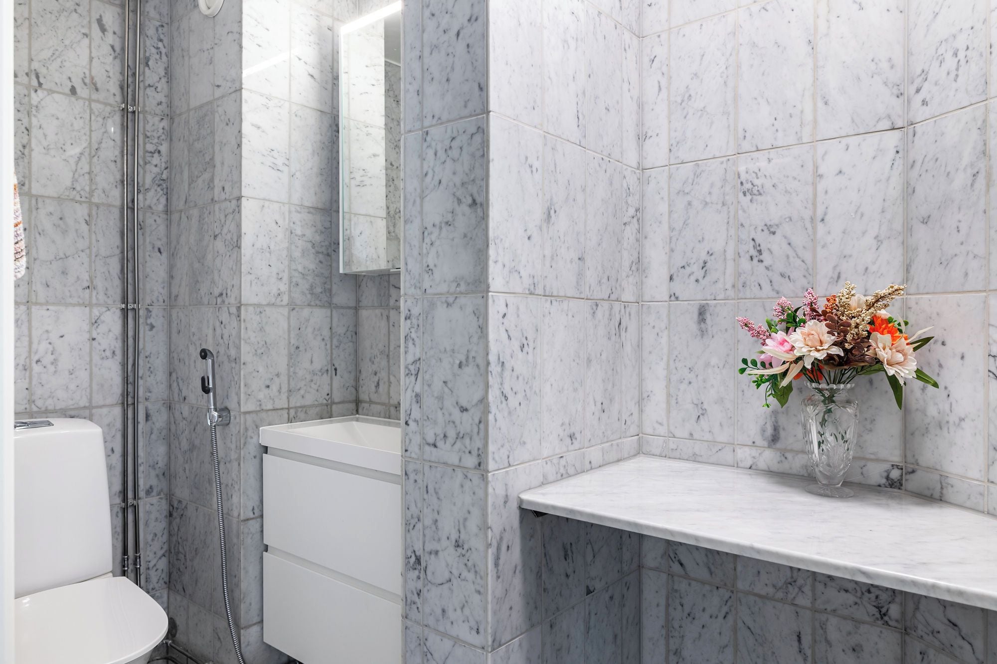 Une salle de bain avec douche, toilettes et un mur en marbre.