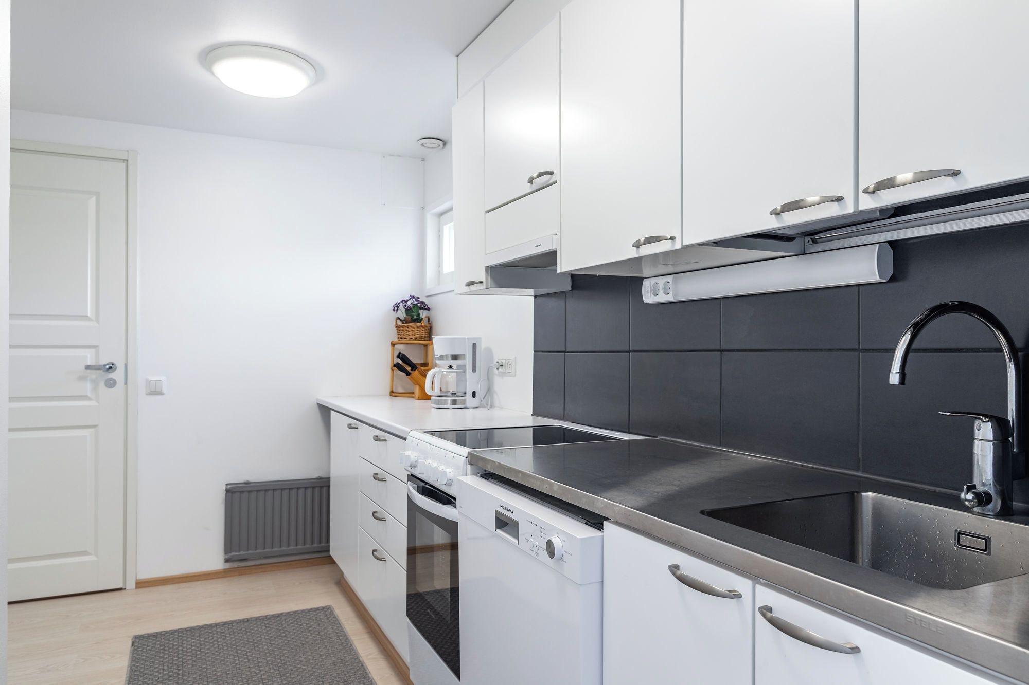 A modern kitchen with white cabinets, a stainless steel sink, and a built-in oven.
