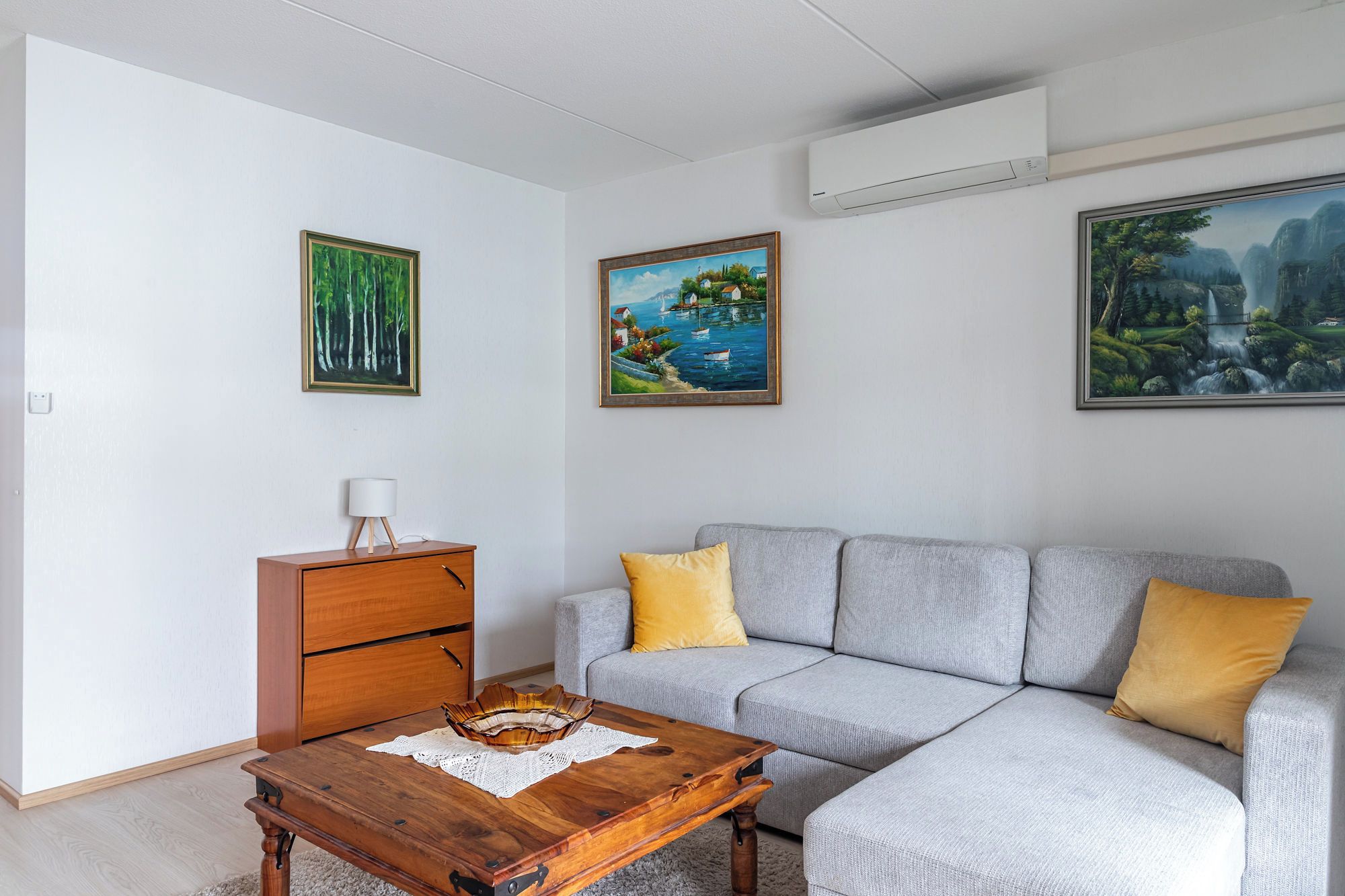Un salon avec un canapé gris, une table basse en bois et un appareil de climatisation blanc fixé au mur.
