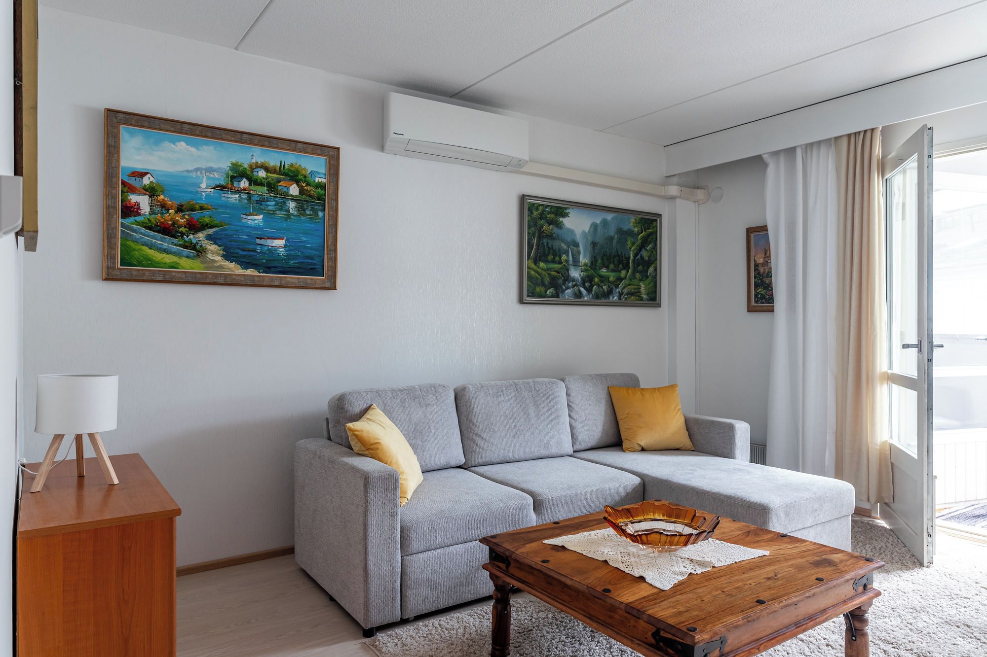A modern living room with a grey sofa, a wooden coffee table, and two paintings on the wall.