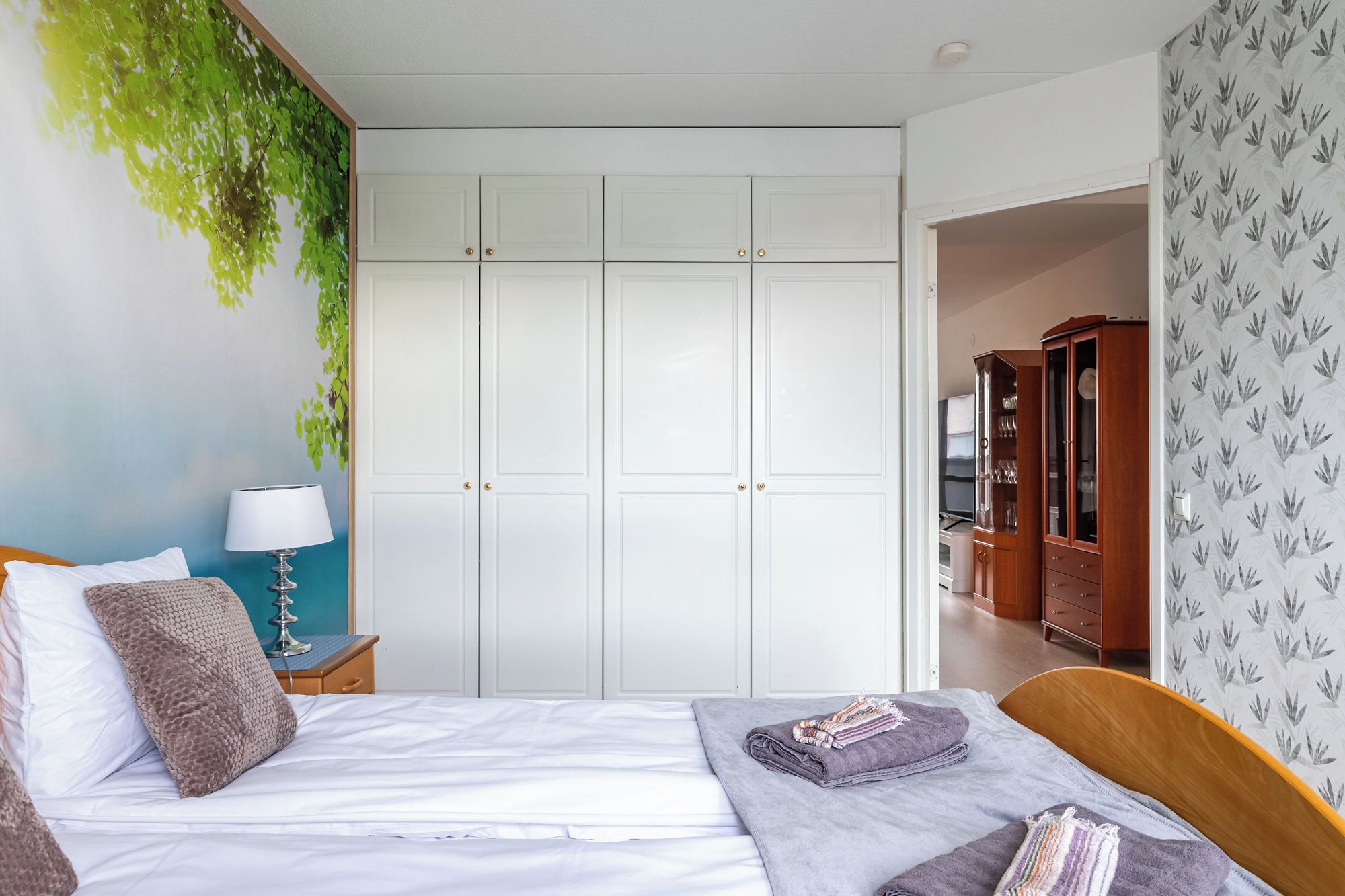 Une chambre d’hôtel avec un lit, une table de chevet, une lampe, une armoire et une vue sur le couloir.