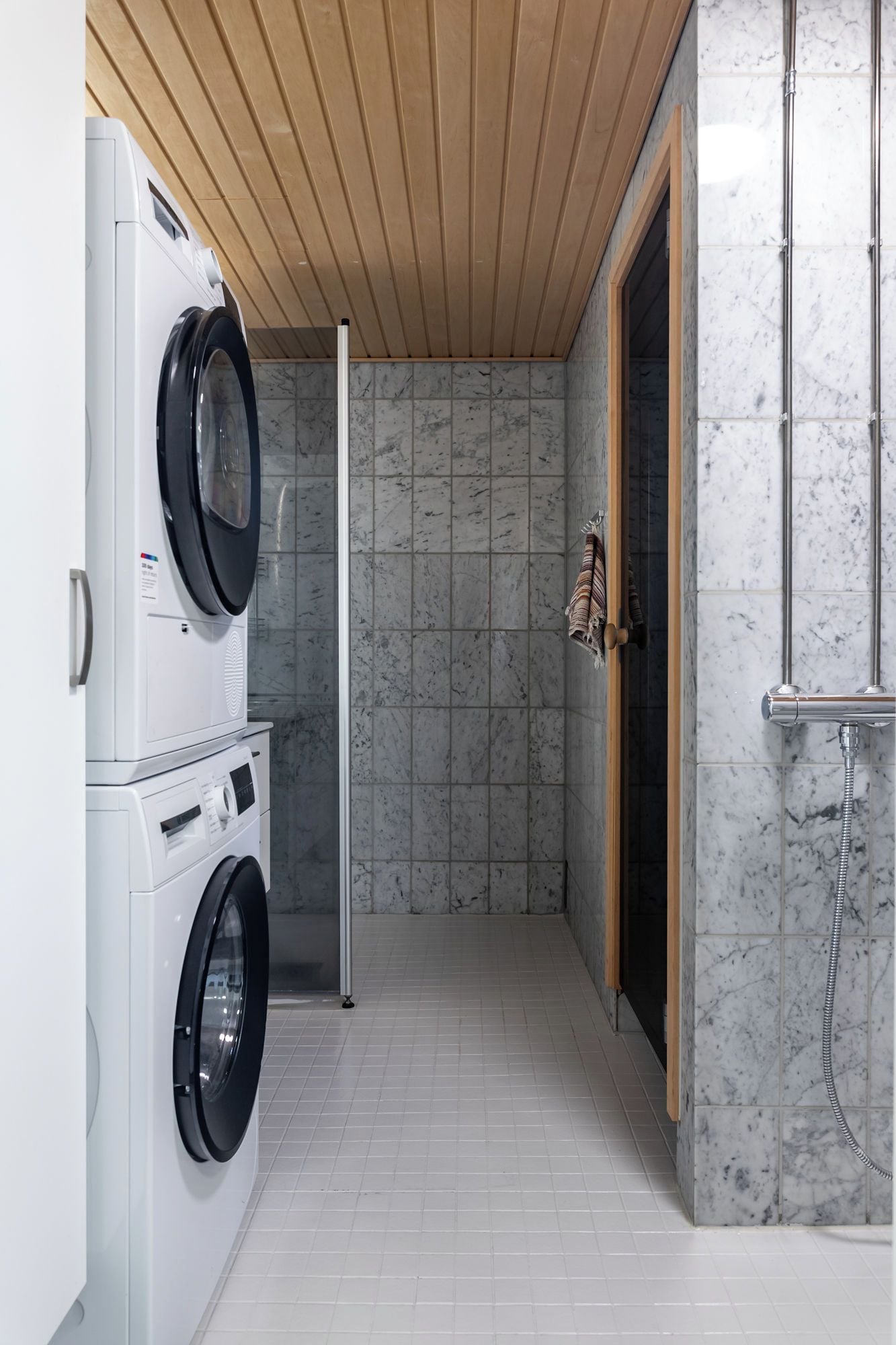 A laundry room with stacked washing machines and a shower area.