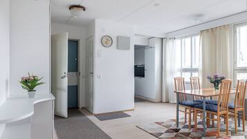 A modern kitchen with white cabinets, a clock on the wall, and a dining area with wooden chairs and a table.