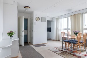 A modern kitchen with white cabinets, a clock on the wall, and a dining area with wooden chairs and a table. - 1BR Downtown Apt with Sauna & Balcony (Lahti)