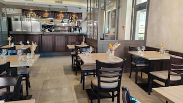 Interno di un ristorante con tavoli, sedie e zona bar.