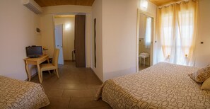 A hotel room with two beds, a desk with a television, a bathroom, and a shower area.