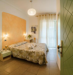 A hotel room with a large bed, bedside tables, a desk, and a view of the outside through curtains.