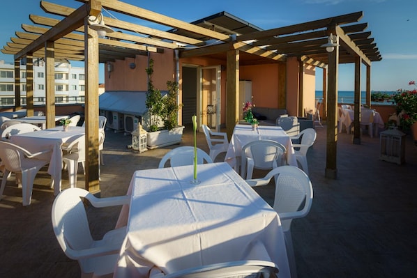 An outdoor patio with tables and chairs, a pergola, and a view of the sea.