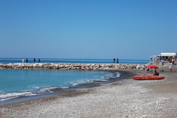 A pebble beach with a rocky breakwater, calm sea, and a lifeguard station.