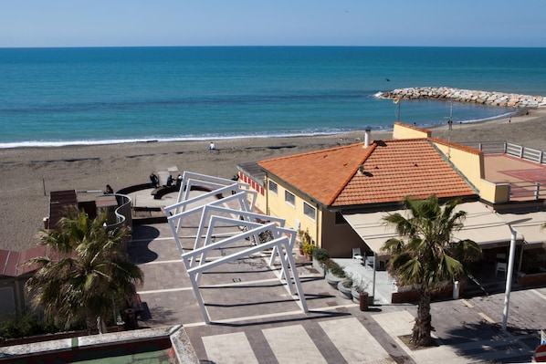A coastal hotel with a beach view, a pool, and a patio area with palm trees.