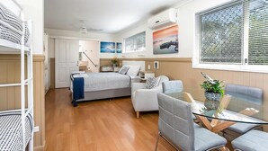 A modern interior with a bed, a sofa, a glass table, and a window with blinds.