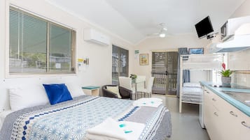 Habitación de hotel compacta con cama, escritorio, silla y kitchenette.