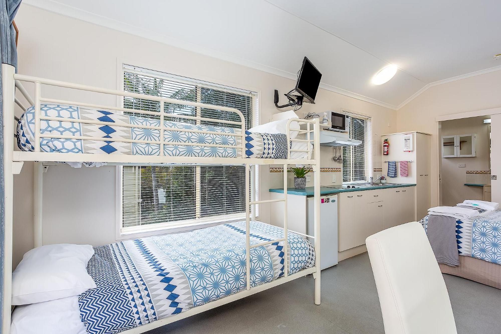 A bunk bed room with a kitchenette, a flat-screen TV, and a bathroom with a mirror and towel rack.