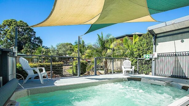 A swimming pool with a hot tub, surrounded by lounge chairs and a shaded area.