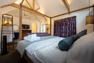Quarto com cama, cabideiro, televisão e janela com cortinas.