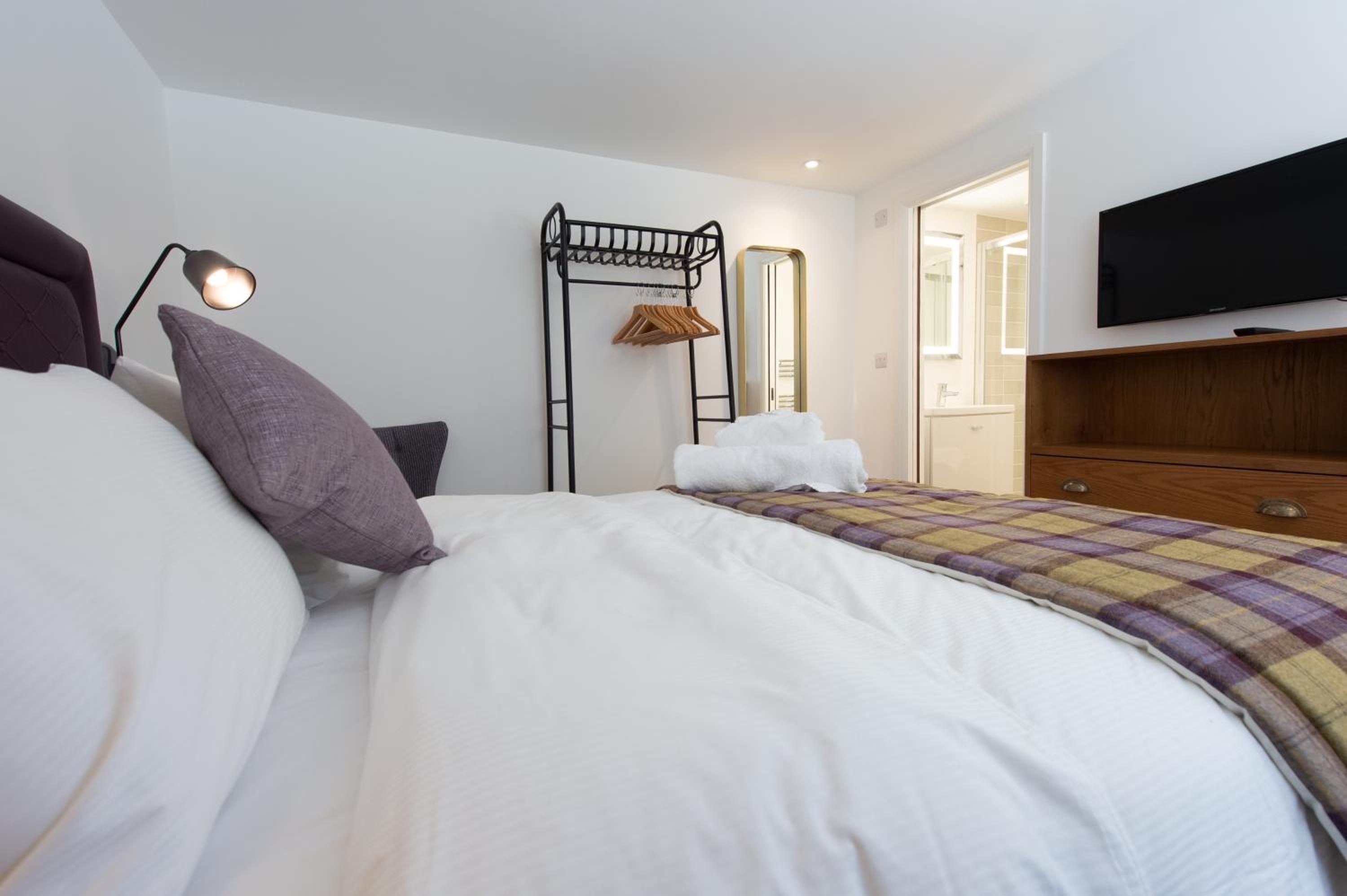 A hotel room with a bed, a bedside lamp, a coat rack, a mirror, and a television.