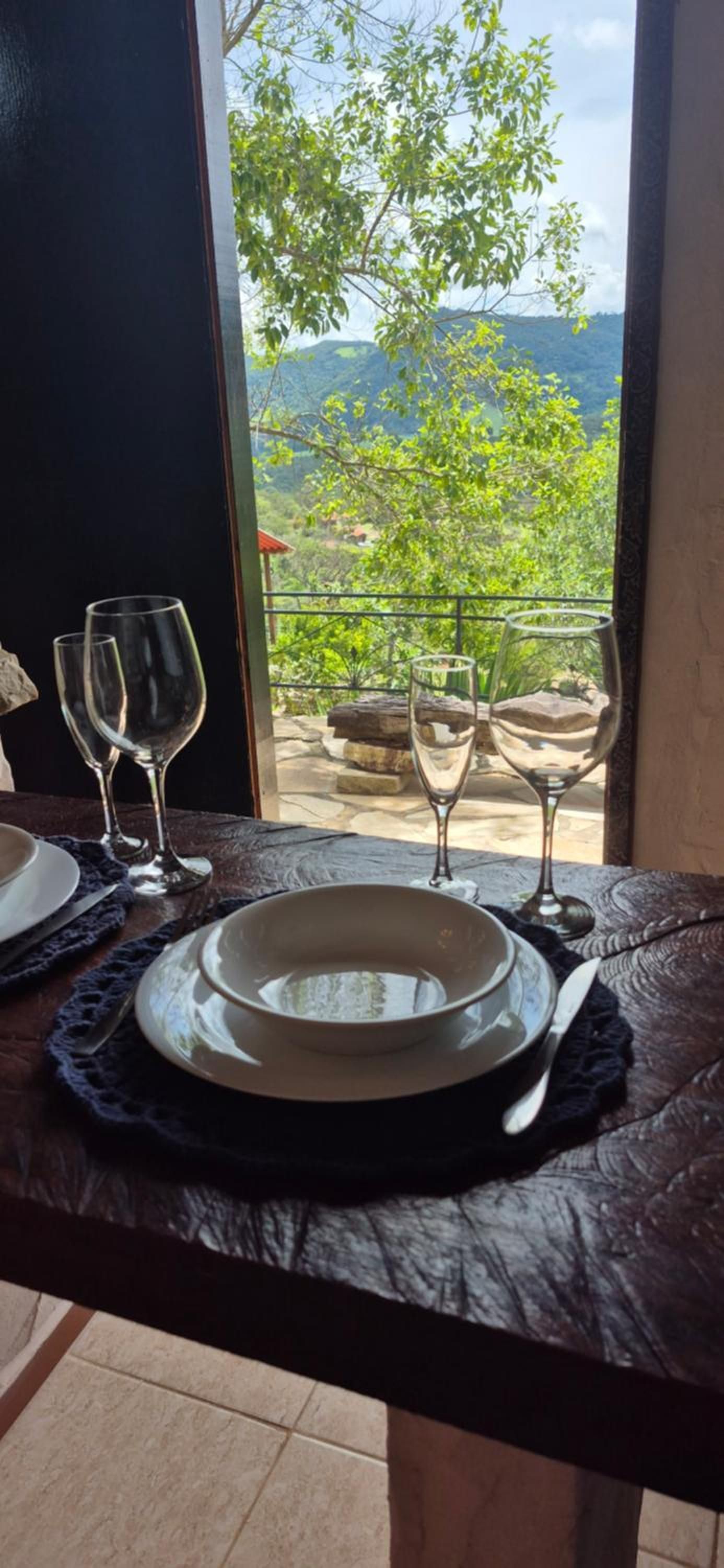 Mesa de jantar com pratos, copos e talheres, com vista para montanhas.