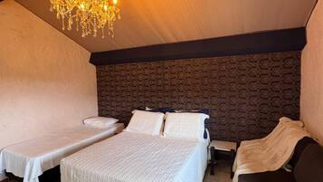 Quarto aconchegante com uma cama grande, duas camas menores, cabeceira escura e um candelabro.