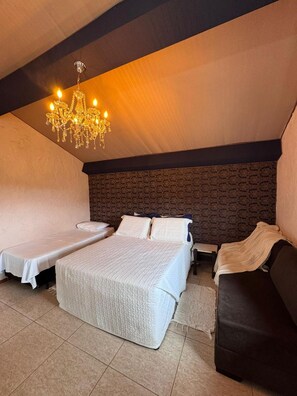 A cozy bedroom with a large bed, two smaller beds, a dark headboard, and a chandelier.