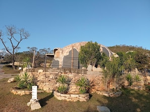 A dome-shaped building with a stone wall in front, surrounded by various plants and a clear sky.