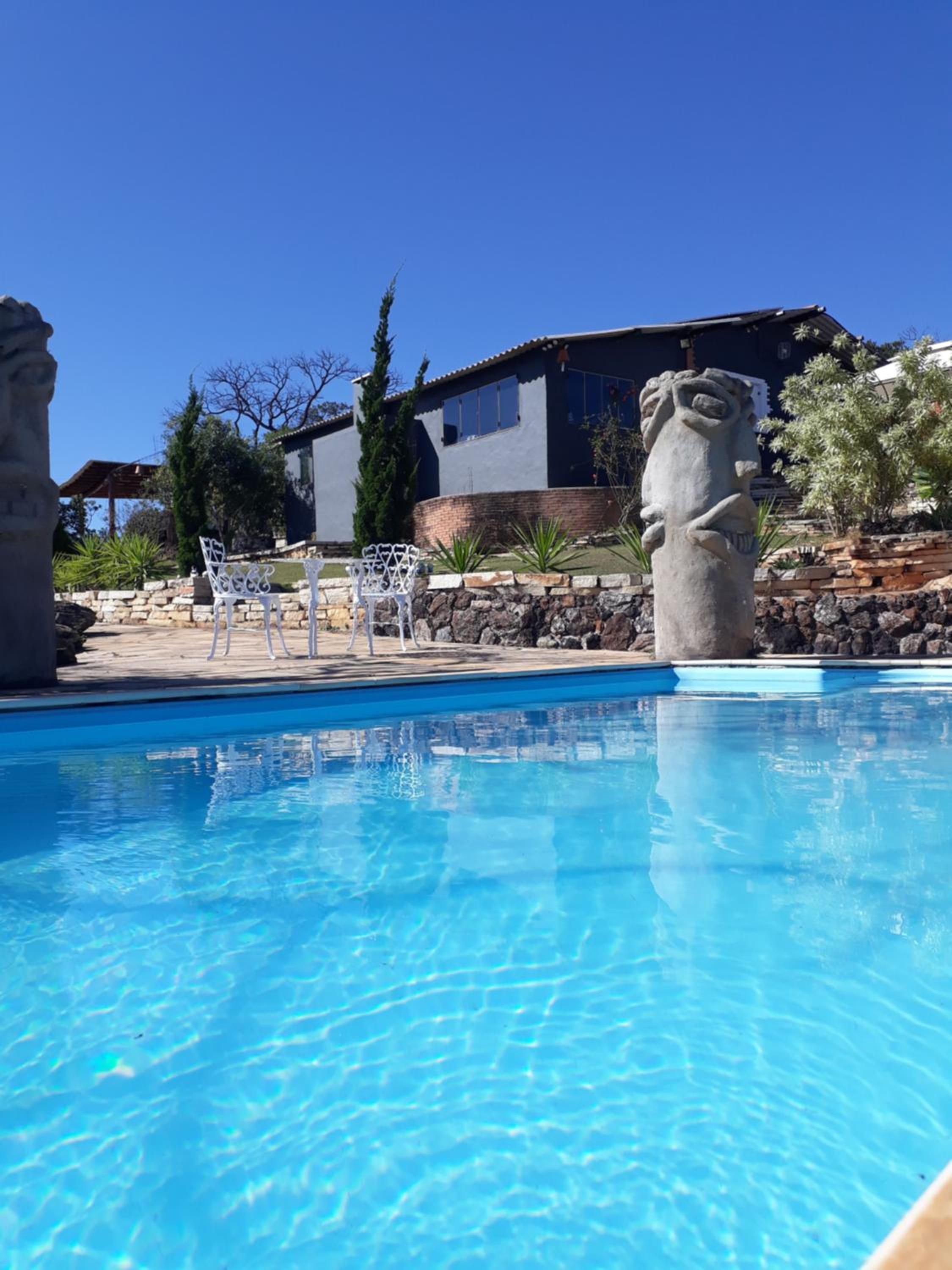 A clear blue pool with white chairs and a stone sculpture.
