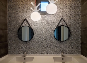 A bathroom with a patterned wall, two sinks, and two round mirrors. - Sous Les Pins (Etoile-sur-Rhone)