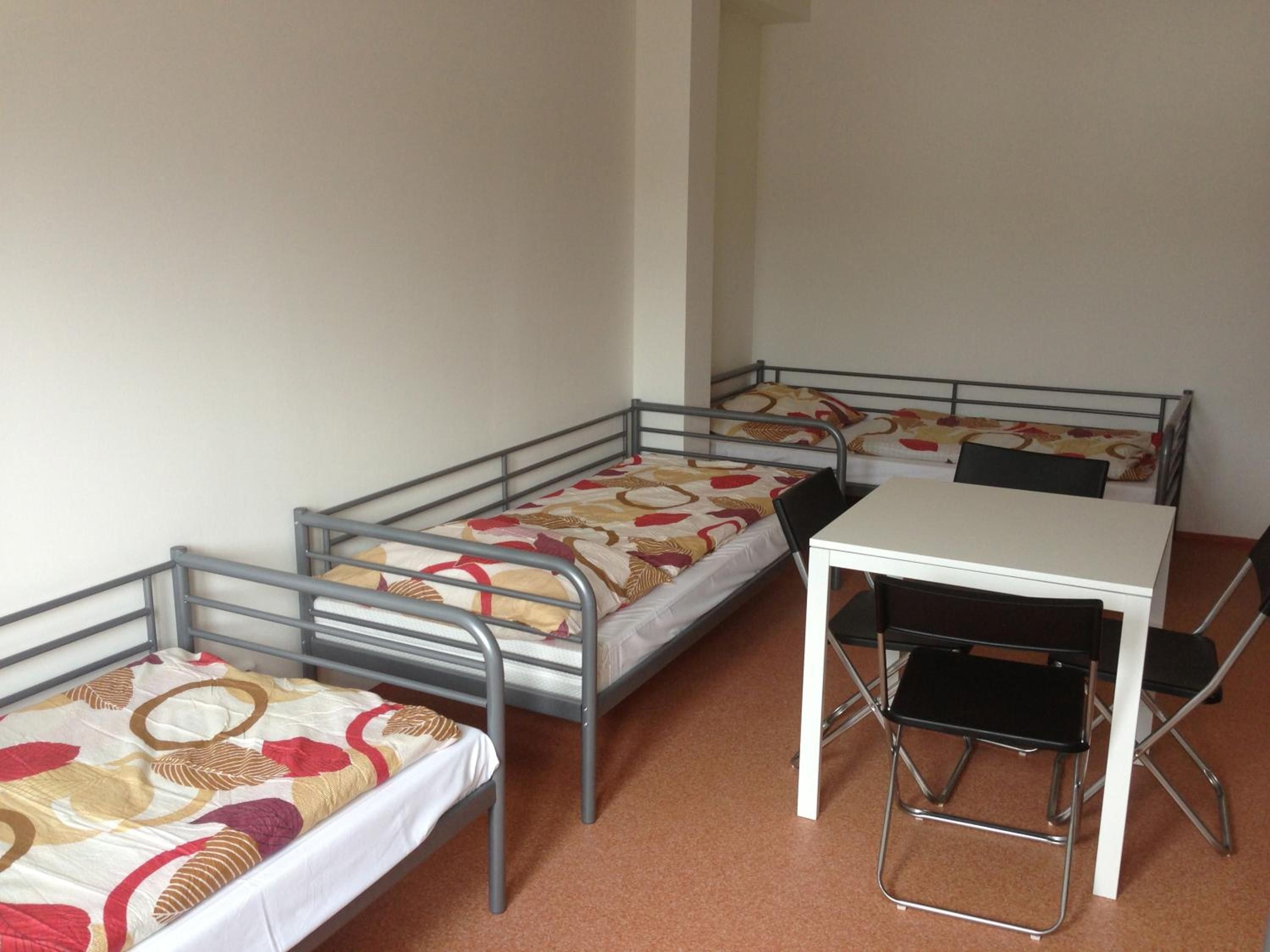 A dormitory room with three metal bunk beds and a white desk with a black chair.