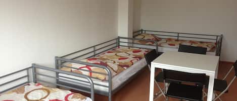 A dormitory room with three metal bunk beds and a white desk with a black chair.