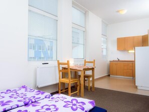 Una habitación con cama, una silla, una mesa, un radiador y una zona de cocina.