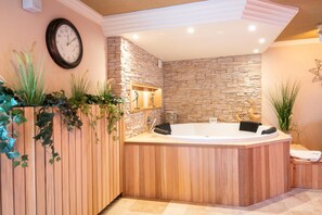 A spa room with a stone wall, wooden paneling, a large bathtub, and a clock on the wall.