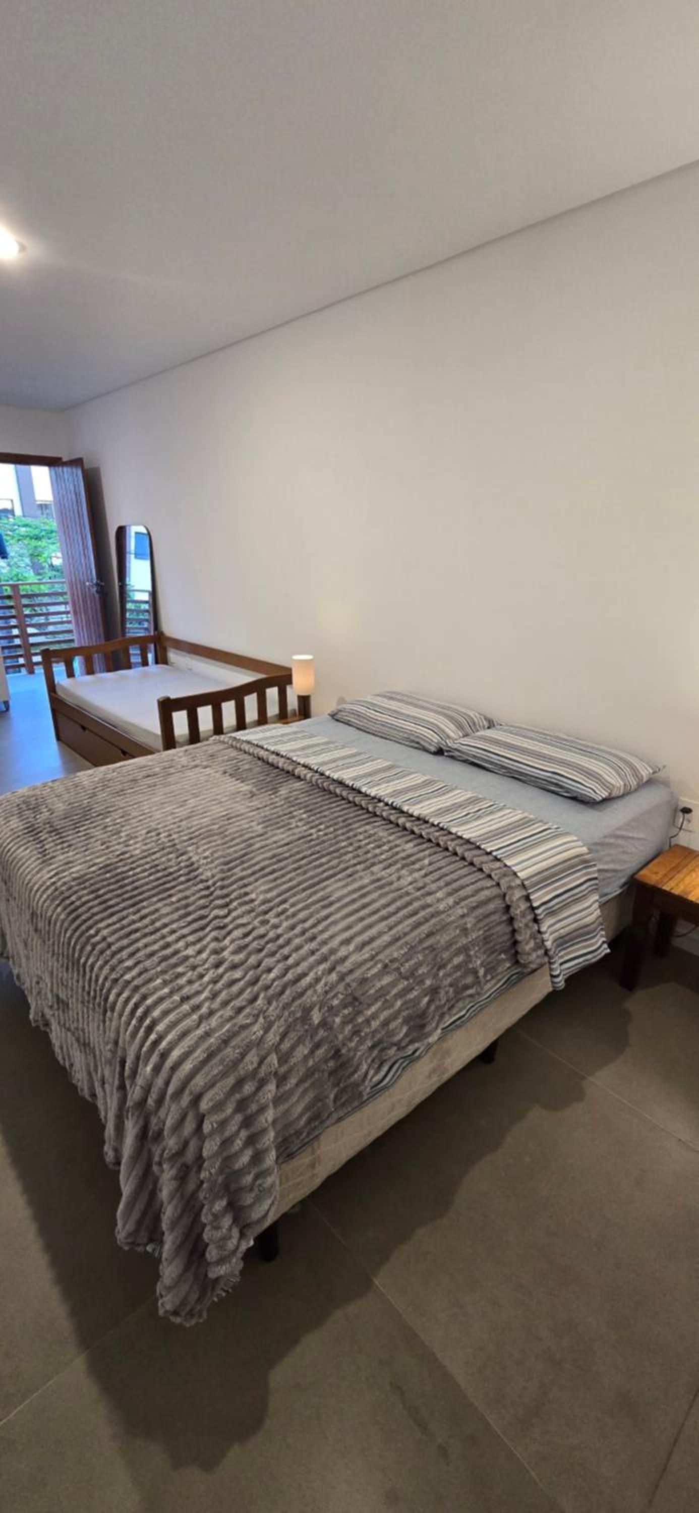 A bedroom with a bed, a wooden chair, a bedside table, and a view of a balcony.
