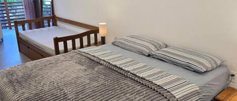 A bedroom with a bed, a wooden chair, a bedside table, and a view of a balcony.