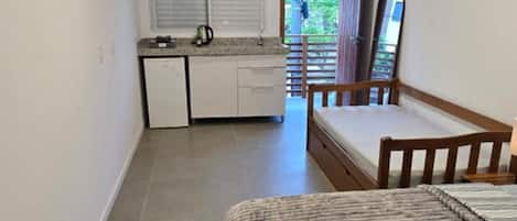 Une petite pièce comprenant un lit, un coin cuisine et donnant sur l’extérieur par une porte.