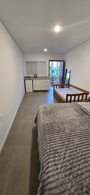 Una habitación pequeña con una cama, kitchenette y vistas a través de una puerta.