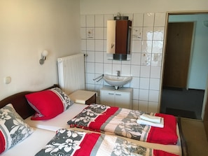 Une chambre d’hôtel comprenant un lit, une table de chevet, un miroir, un radiateur et une salle de bain avec un lavabo et un meuble.