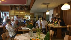 Ein Restaurantinneres mit Holztischen und -stühlen, einem Barbereich und einer Gruppe von Gästen.