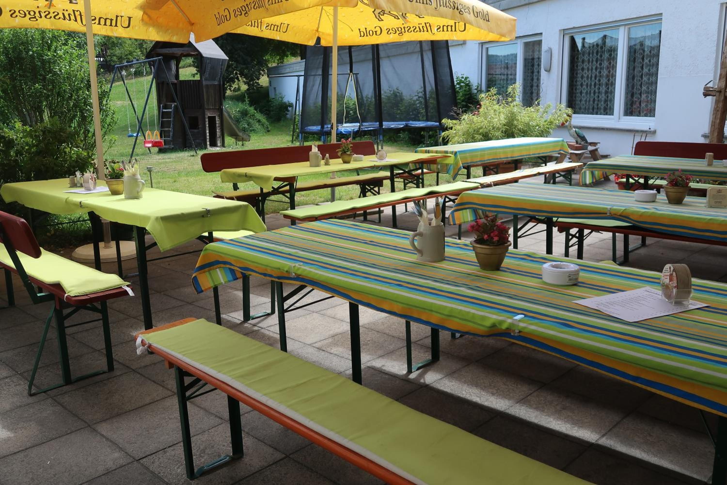 Un área de comedor al aire libre con varias mesas y bancos, cubierta por sombrillas amarillas.