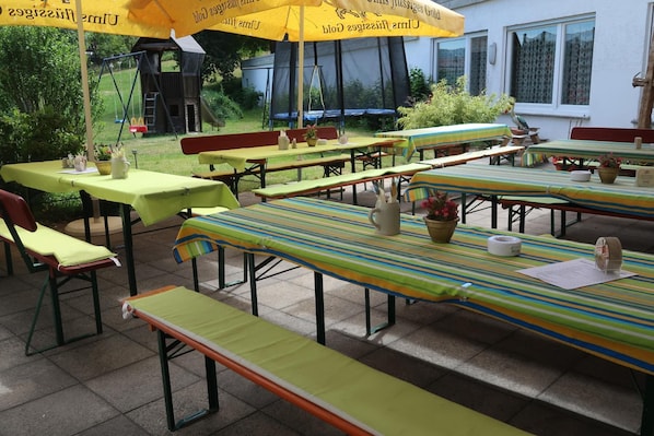 Un espace extérieur aménagé pour les repas, avec plusieurs tables et bancs, protégé par des parasols jaunes.