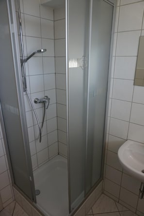 Une cabine de douche fermée par des parois en verre, dotée d’un pommeau de douche à main et d’un robinet fixé au mur.